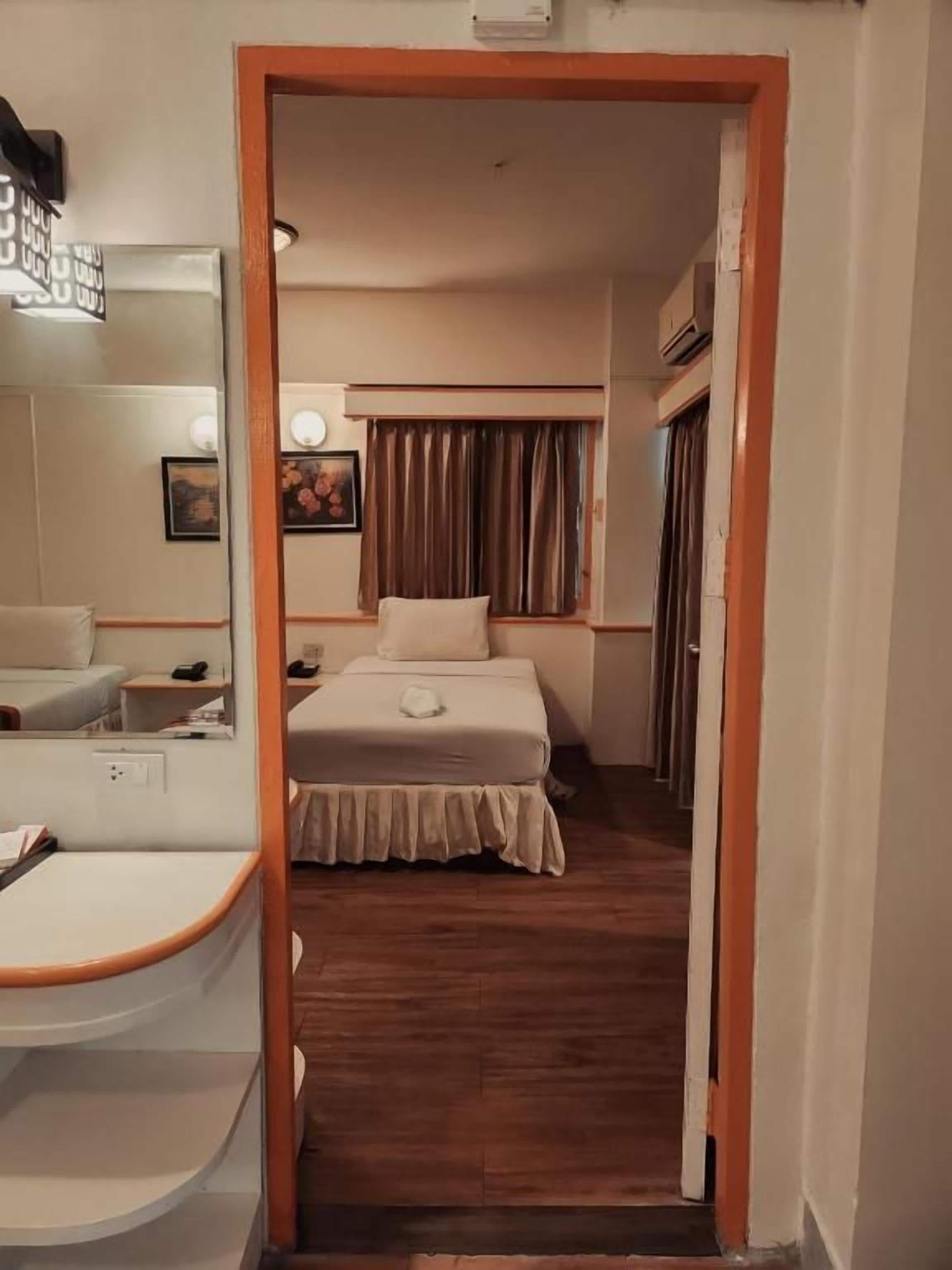 A hotel room with a bed, a bedside table, a mirror, and a wooden floor.
