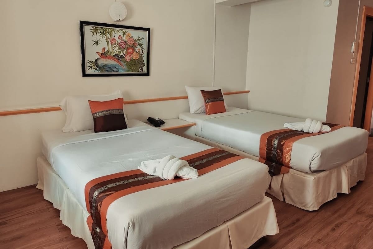 Ein Hotelzimmer mit zwei Betten, jeweils mit weißer Bettdecke und braunen Zierkissen. Über den Betten hängt ein gerahmtes Bild.