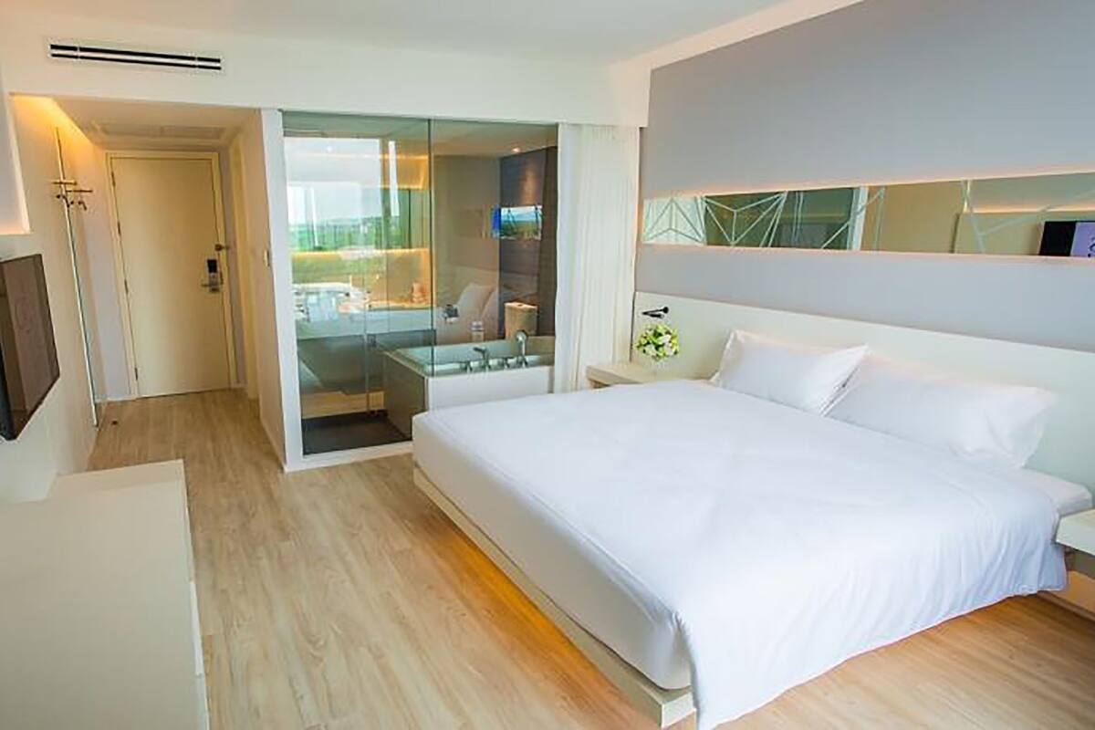Een moderne hotelkamer met een groot bed, een aan de muur bevestigde televisie en een glazen deur naar een badkamer.