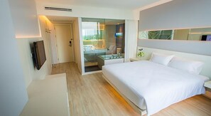 A modern hotel room with a large bed, a TV mounted on the wall, and a glass door leading to a bathroom.