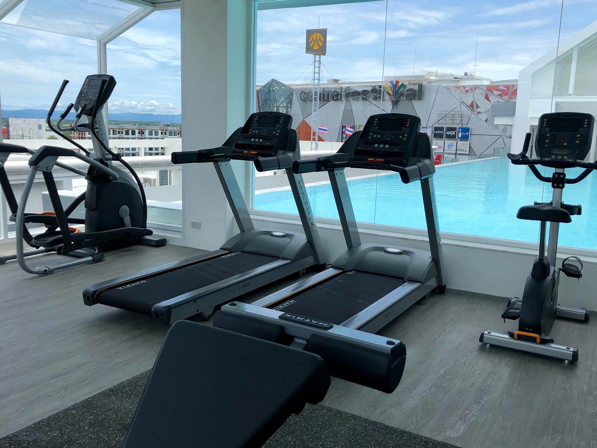 A gym with treadmills, an elliptical, and a rowing machine, overlooking a pool and a view of a cityscape.