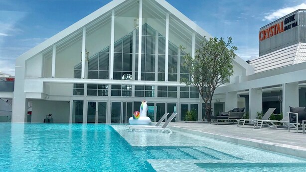 Een modern hotel met een groot zwembad, een glazen gevel en een bord met de tekst 'Crystal Hotel'.