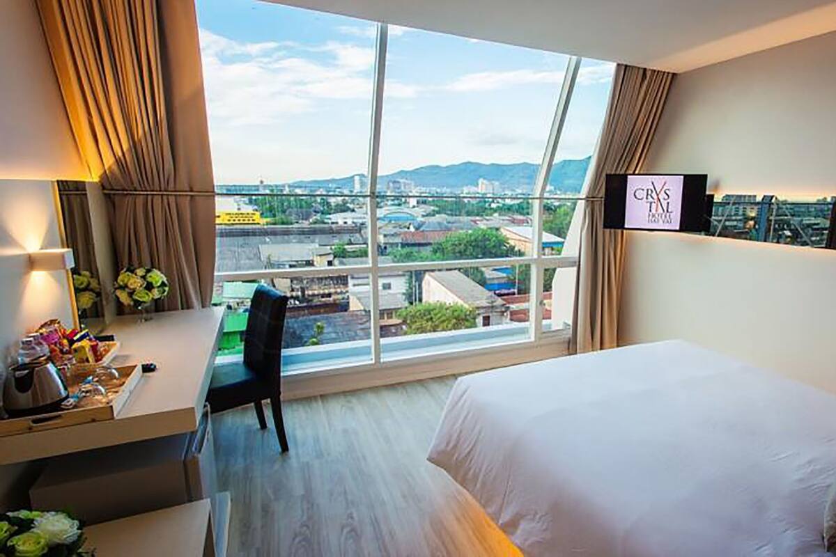Hotelkamer met een groot raam, een bed, een bureau met stoel en een televisie aan de muur.
