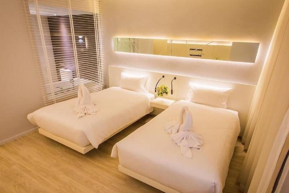 Een hotelkamer met twee bedden, een nachtkastje met een lamp en een grote spiegel boven de bedden.