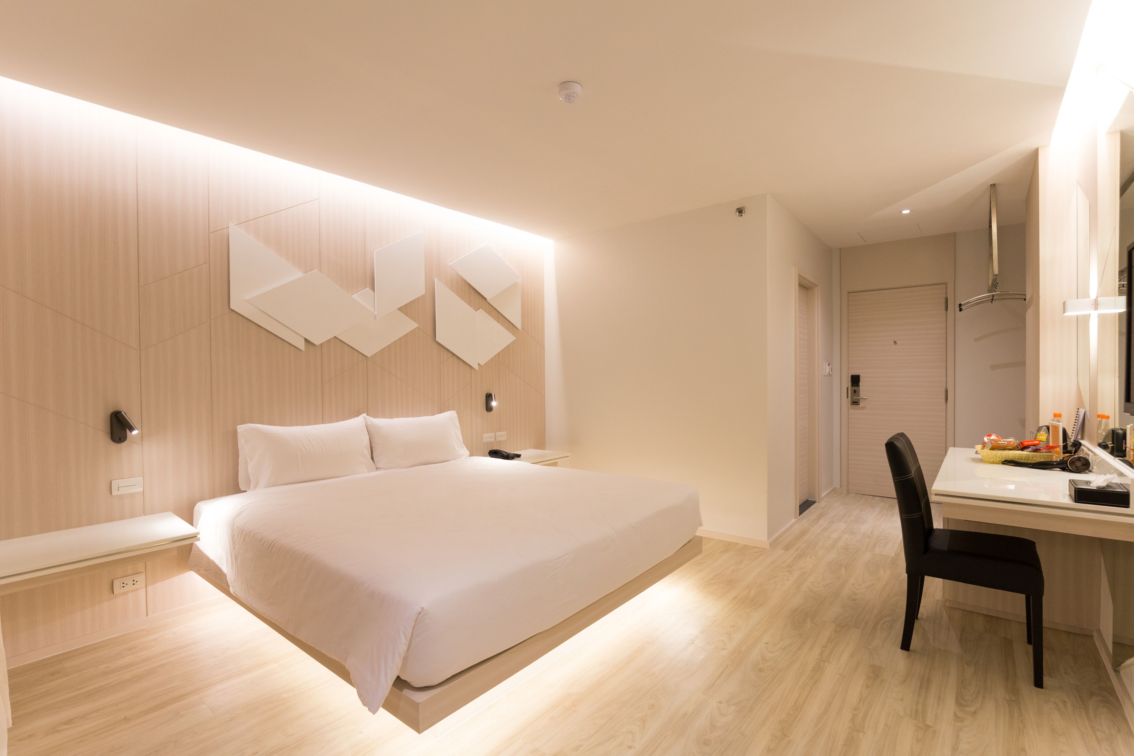 A modern hotel room with a large bed, a desk with a chair, and a mirror.