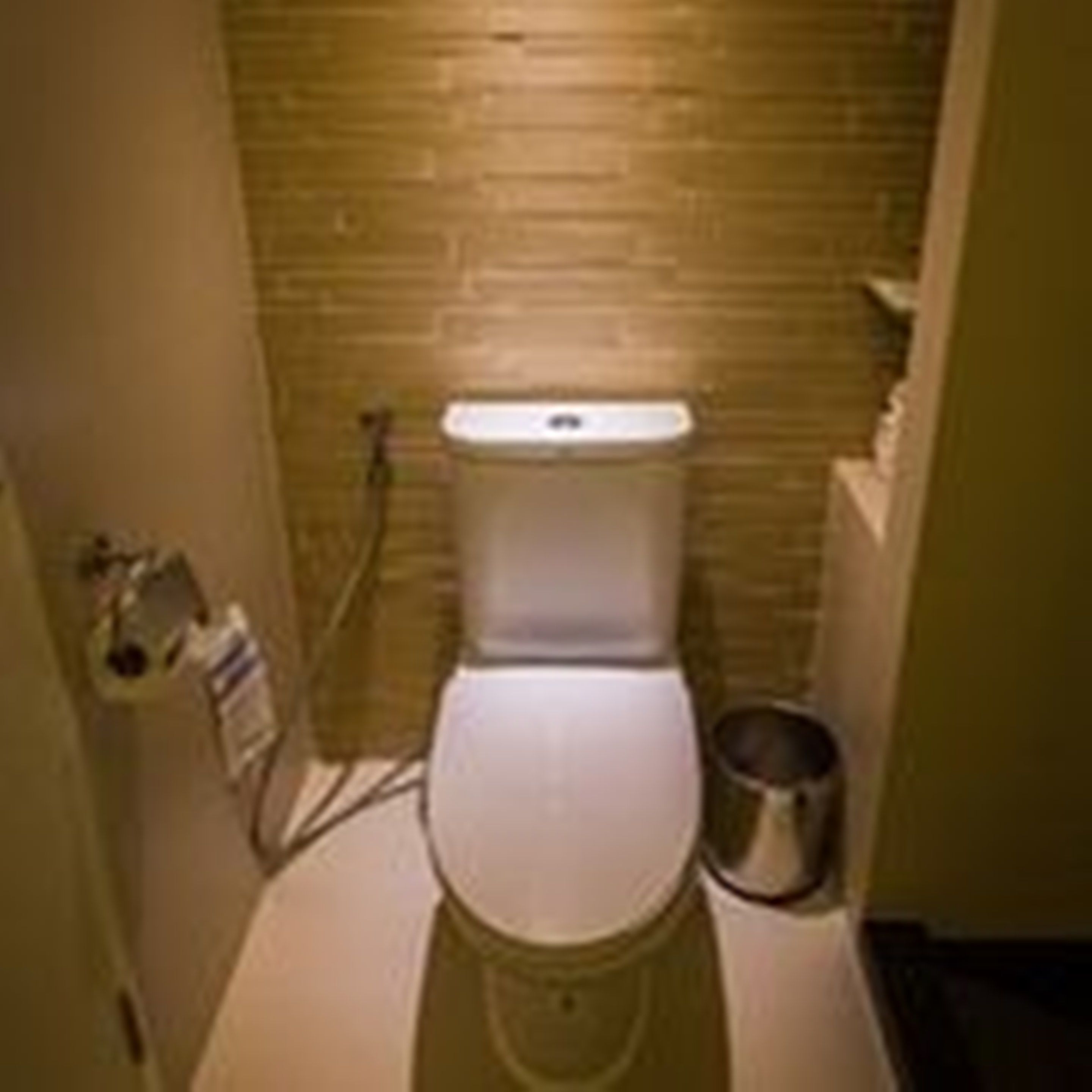 A small, compact bathroom with a white toilet, a trash can, and a wall-mounted sink.