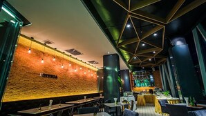 Een modern restaurantinterieur met zichtbare bakstenen muren, hangende吊灯和 geometrisch plafond. Tafels zijn klaar voor diners.