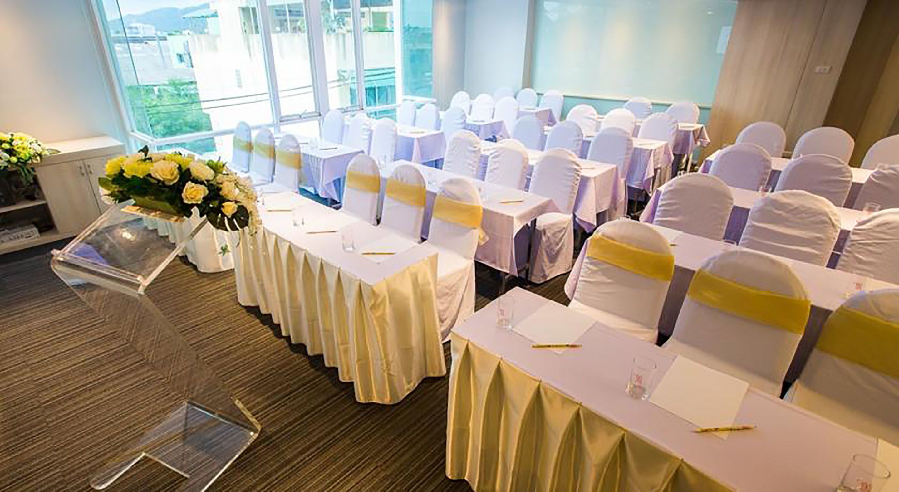 A conference room with rows of tables and chairs, each with a white tablecloth and yellow sashes.