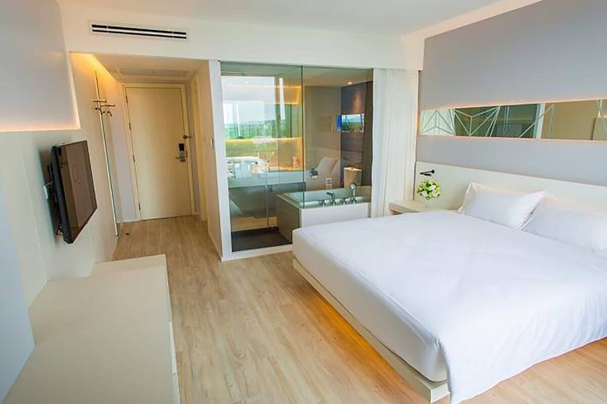 Een moderne hotelkamer met een groot bed, een aan de muur bevestigde televisie en een glazen deur naar een badkamer.