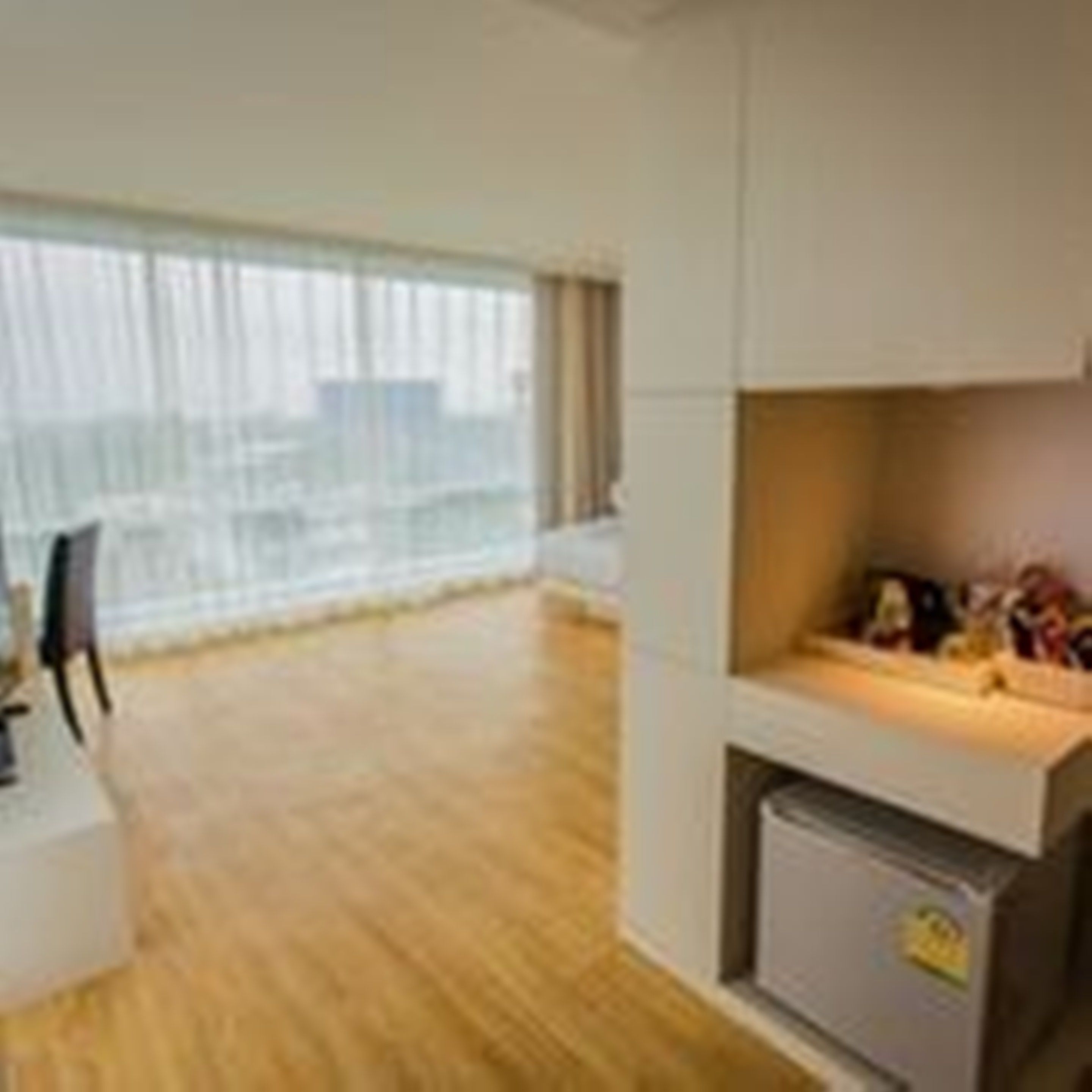 A modern living room with a wooden floor, a sofa, a dining table, and a kitchen area with a refrigerator.