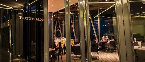 Vista interior de un restaurante con diseño moderno, que incluye divisiones de vidrio y un área de comedor visible con mesas y sillas.