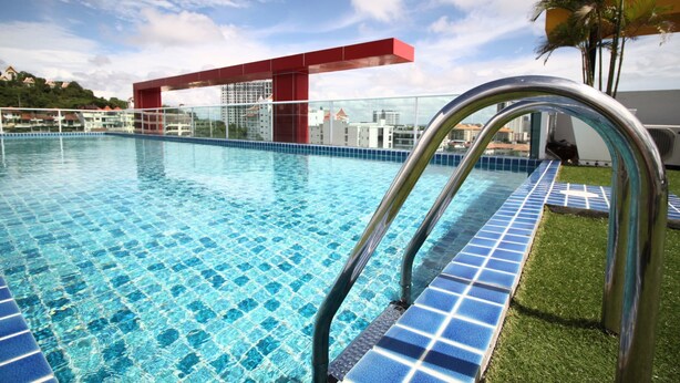 A swimming pool with clear blue tiles, metal handrails, and a view of buildings in the background. - Art on The Hill by PSR ASIA (Pattaya)