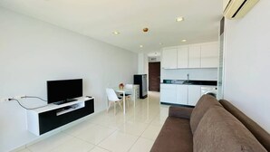 A modern living room with a flat-screen TV, a sofa, and a dining area with a table and chairs. - Art on The Hill by PSR ASIA (Pattaya)