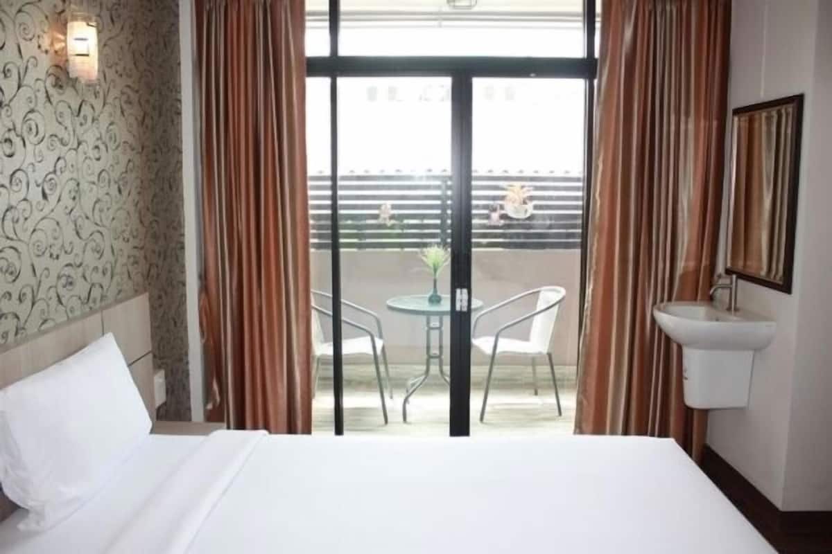 A hotel room with a bed, a small table with chairs, a sink, and a view of the outside balcony.