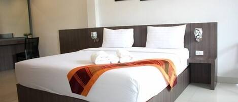 A neatly made bed with white linens and a decorative orange and red throw blanket. There are two wall-mounted nightstands with decorative items on them.
