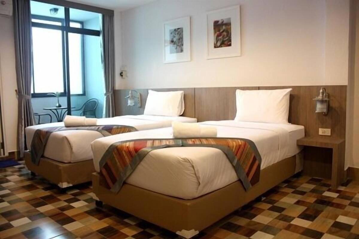A hotel room with two beds, a checkered floor, a window with curtains, and wall-mounted lights.