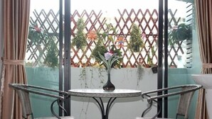 A room with a round table, two chairs, a vase with flowers, and a view through a lattice window. - P'Residence (Hat Yai)