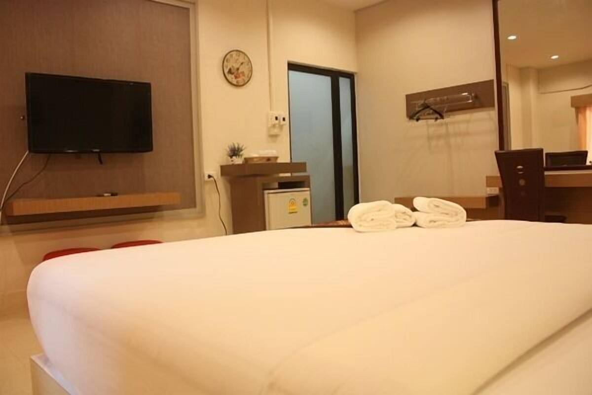 A hotel room with a large bed, a flat-screen TV mounted on the wall, a desk with a computer, and a small refrigerator.
