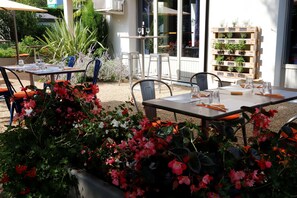 An outdoor dining area with tables and chairs, surrounded by potted plants and a wooden planter with various herbs. - Campanile Grenoble Sud - Saint Martin D'hères (Saint-Martin-d'Heres)