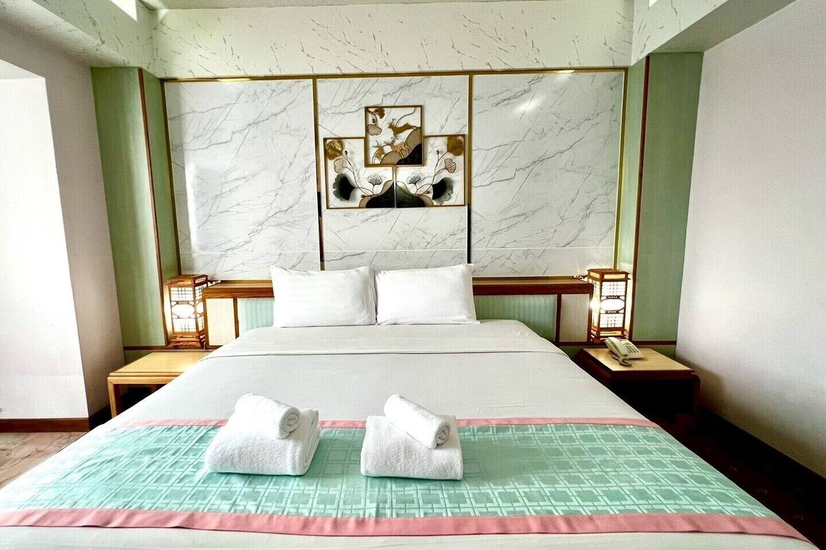 Habitación de hotel con una cama grande, dos mesitas de noche, una silla y una pared con un panel decorativo.