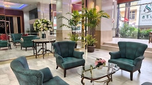 Un hall d’entrée avec des fauteuils verts, une table basse en verre et des plantes en pot.