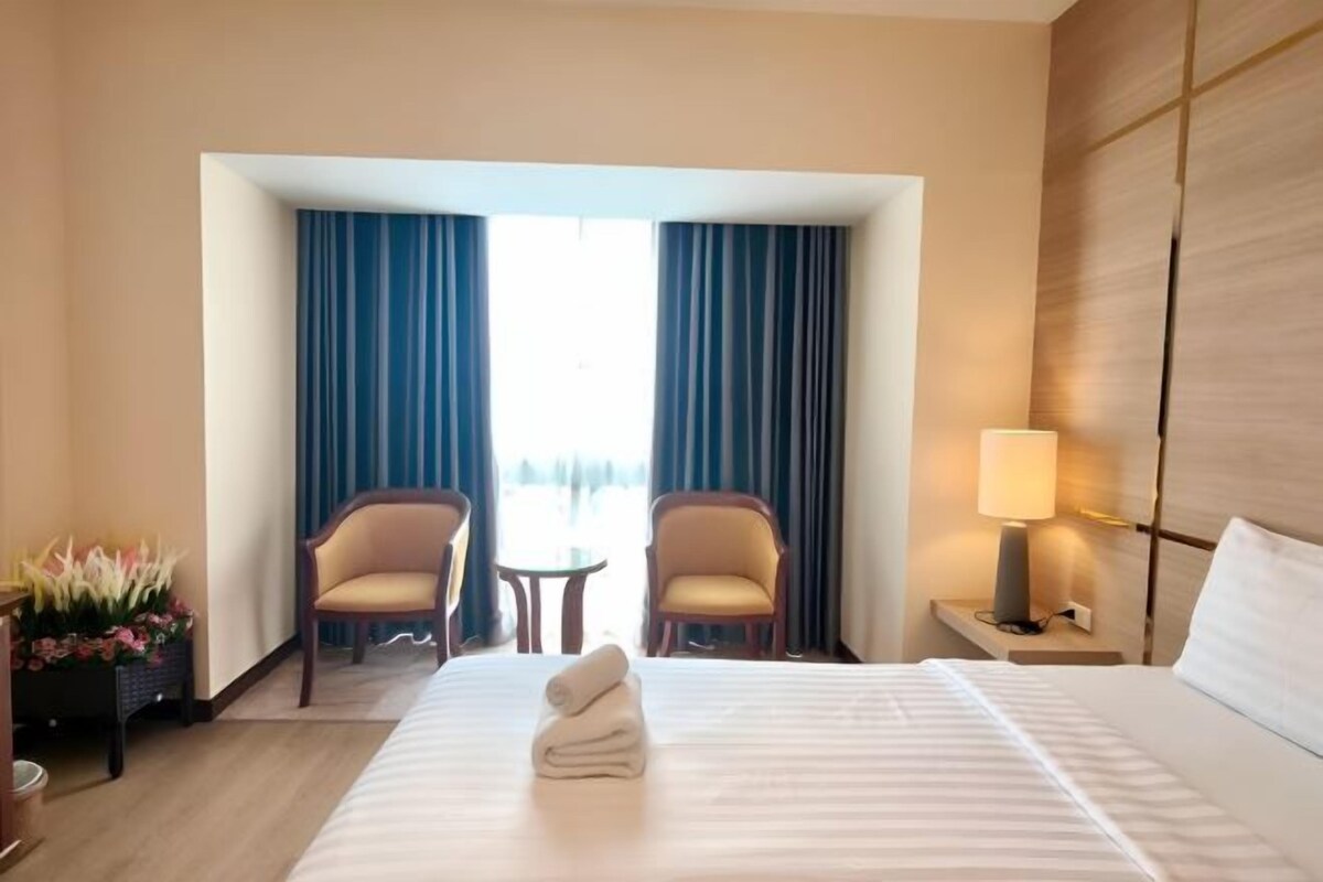 Habitación de hotel con cama, dos sillones, una mesita, lámpara y vistas al exterior.
