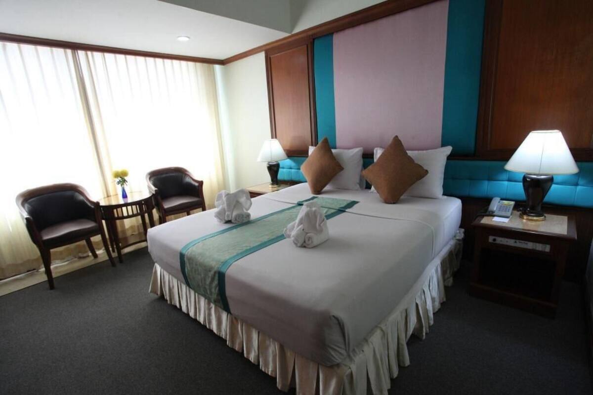 Habitación de hotel con una cama grande, dos mesitas de noche, un escritorio con silla y una ventana con cortinas.