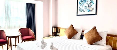 Habitación de hotel con una cama, dos sillas rojas, una mesa y un cuadro en la pared.