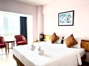 Habitación de hotel con una cama, dos sillas rojas, una mesa y un cuadro en la pared.