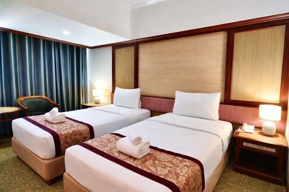 Una habitación de hotel con dos camas, una silla, una mesita de noche y una lámpara.