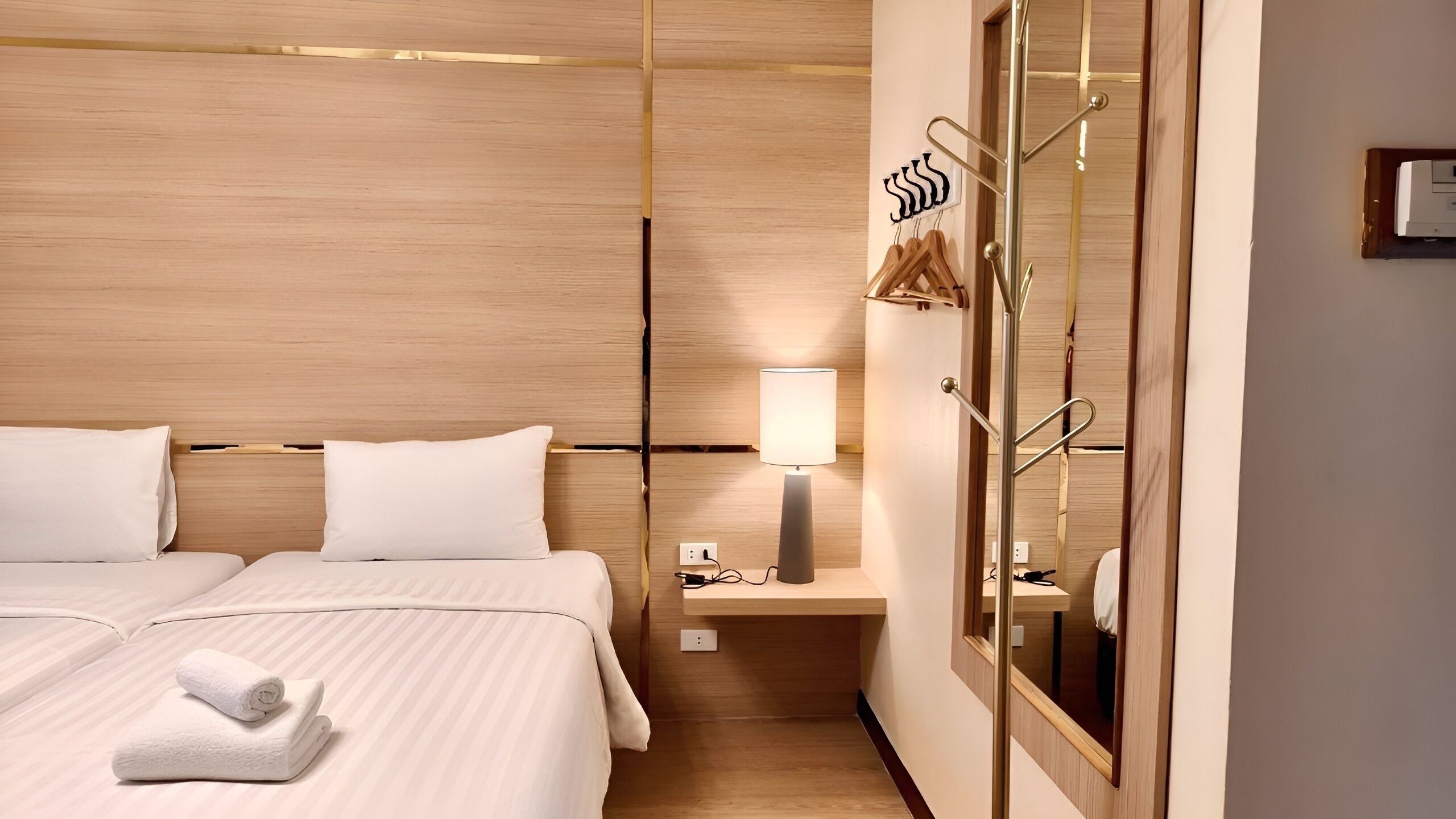 A hotel room with a bed, a bedside table with a lamp, a mirror, and a coat rack.