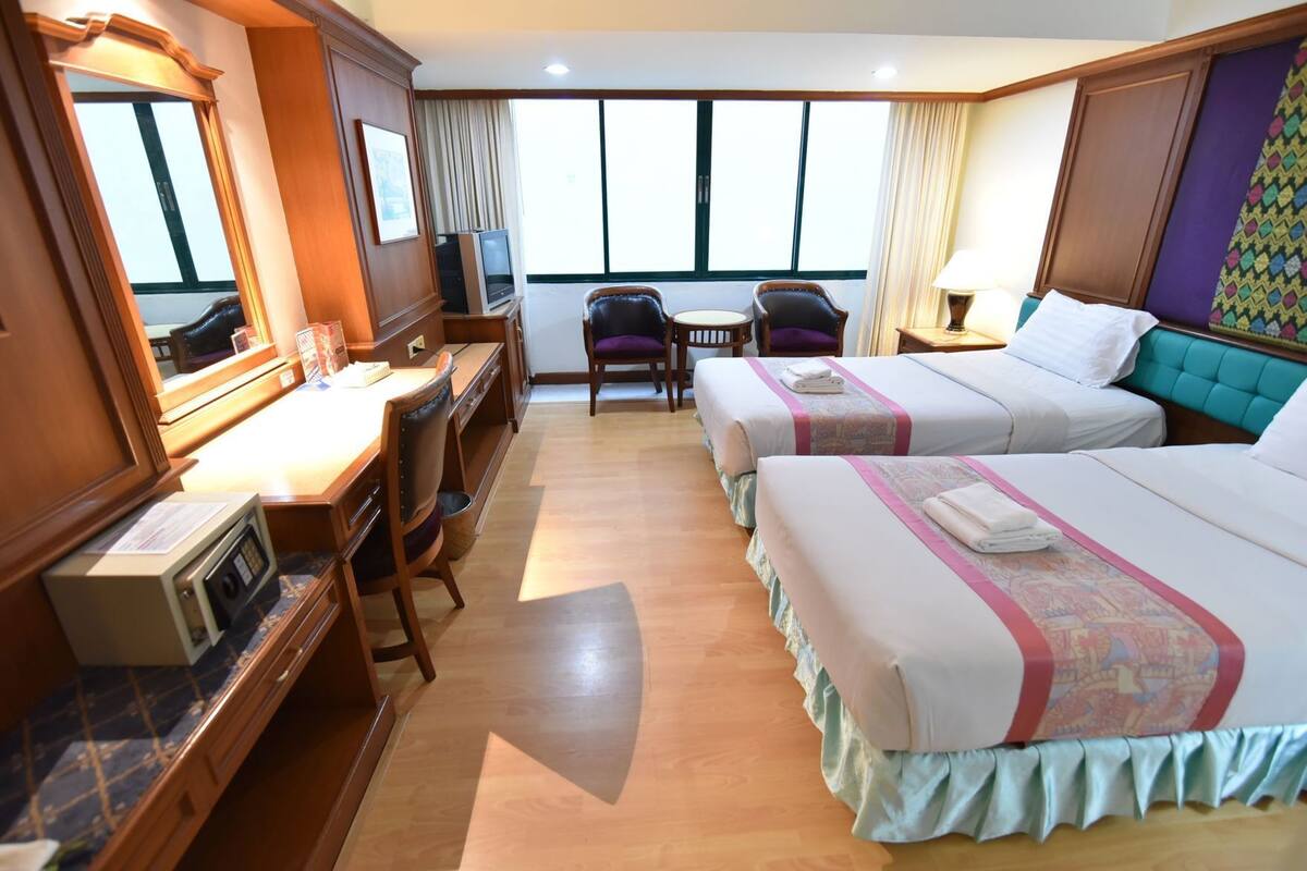 Habitación de hotel con dos camas, un escritorio con ordenador, una silla y televisión.