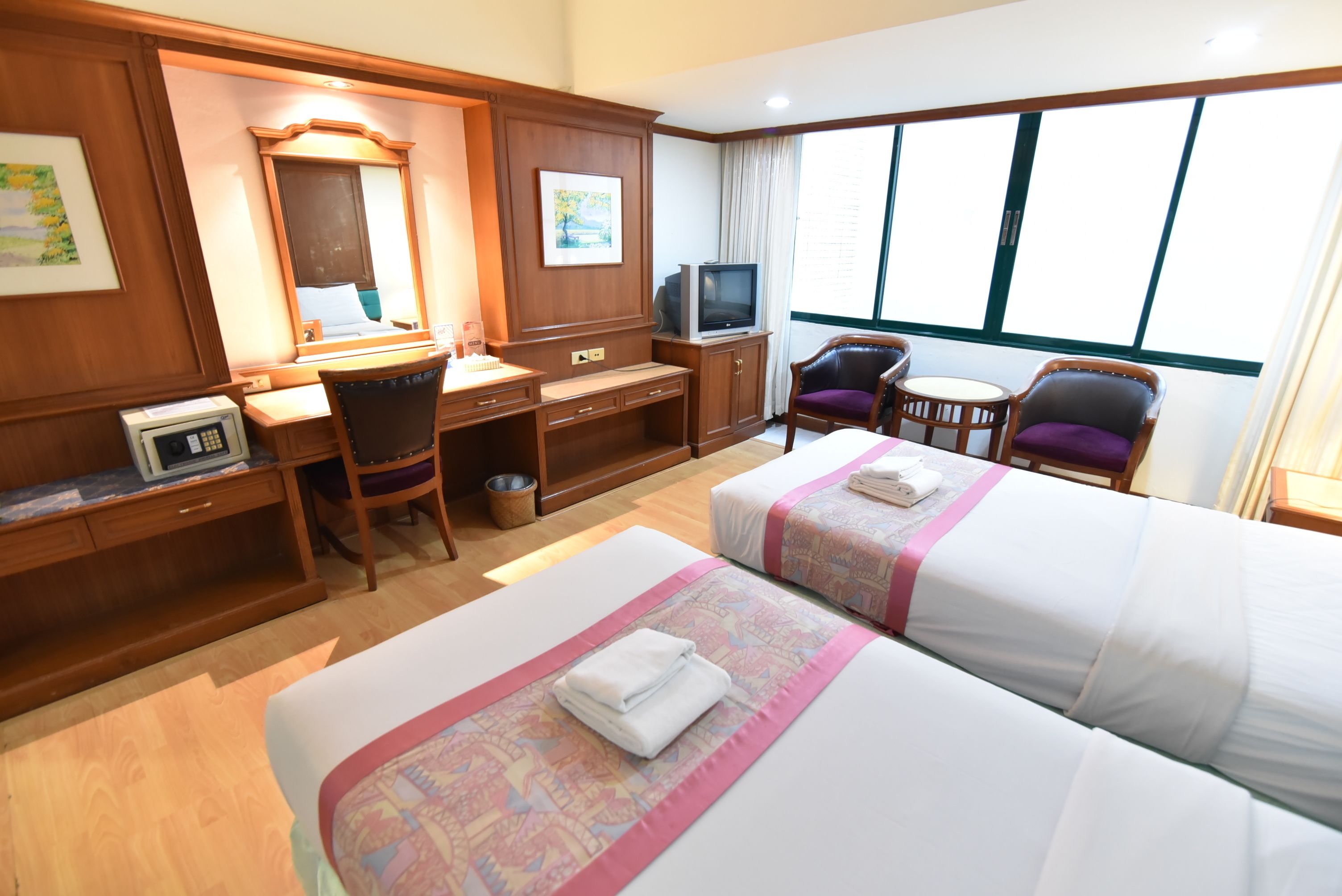 Habitación de hotel con dos camas, un escritorio, televisión, una silla y un ventanal grande.