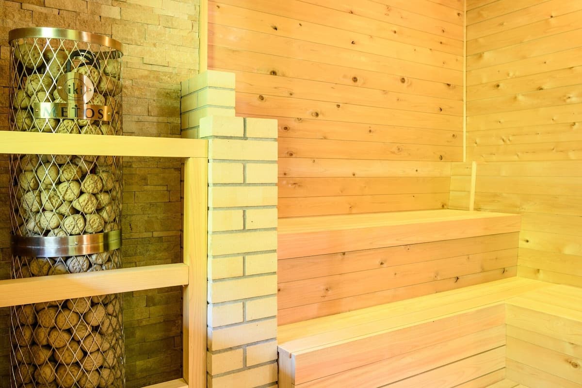 Sauna, jonka seinät ovat puuta, ja metallinen säiliö, jossa on puita.