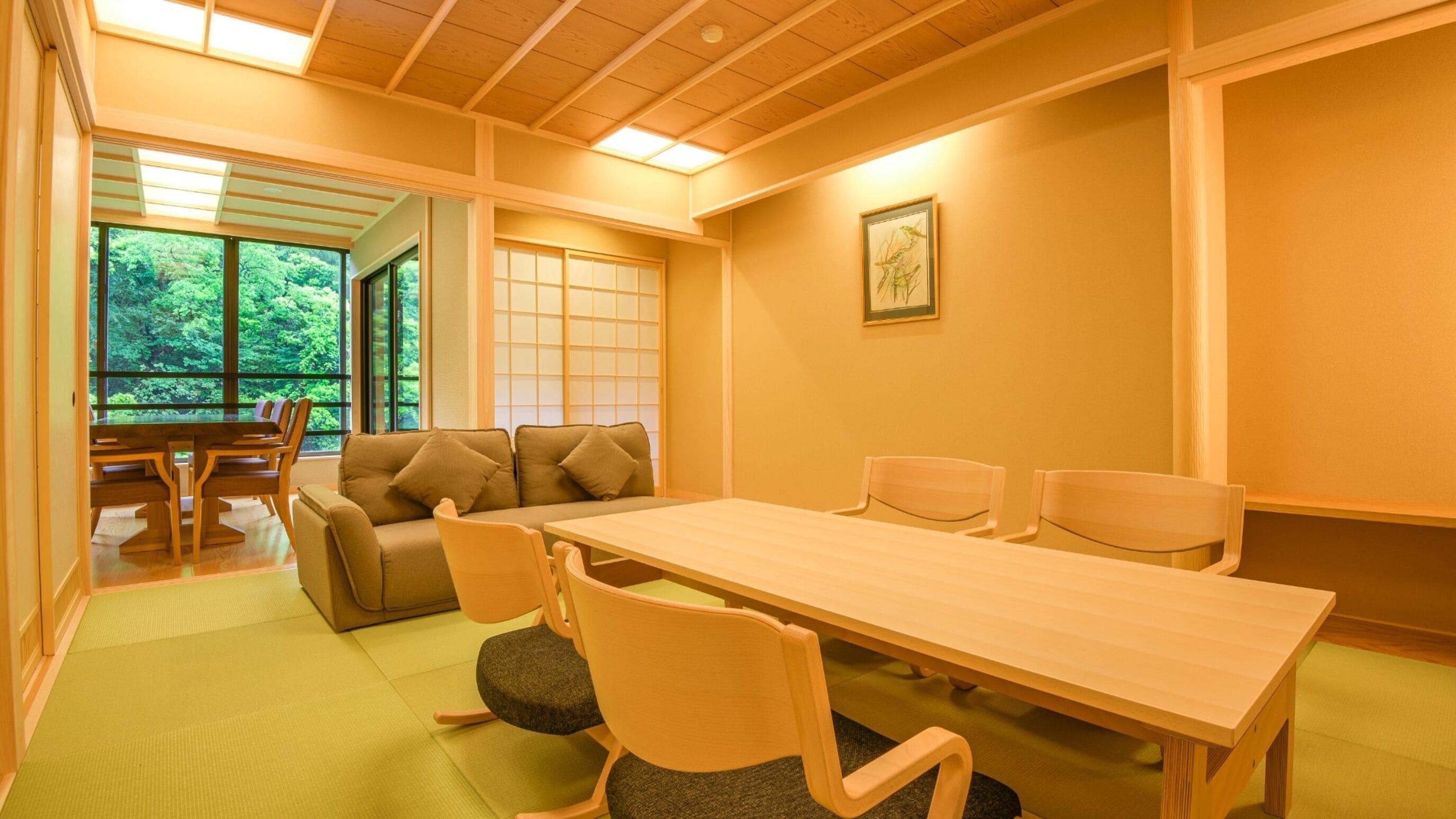 A room with a wooden table, four chairs, a sofa, and a window with a view of greenery.