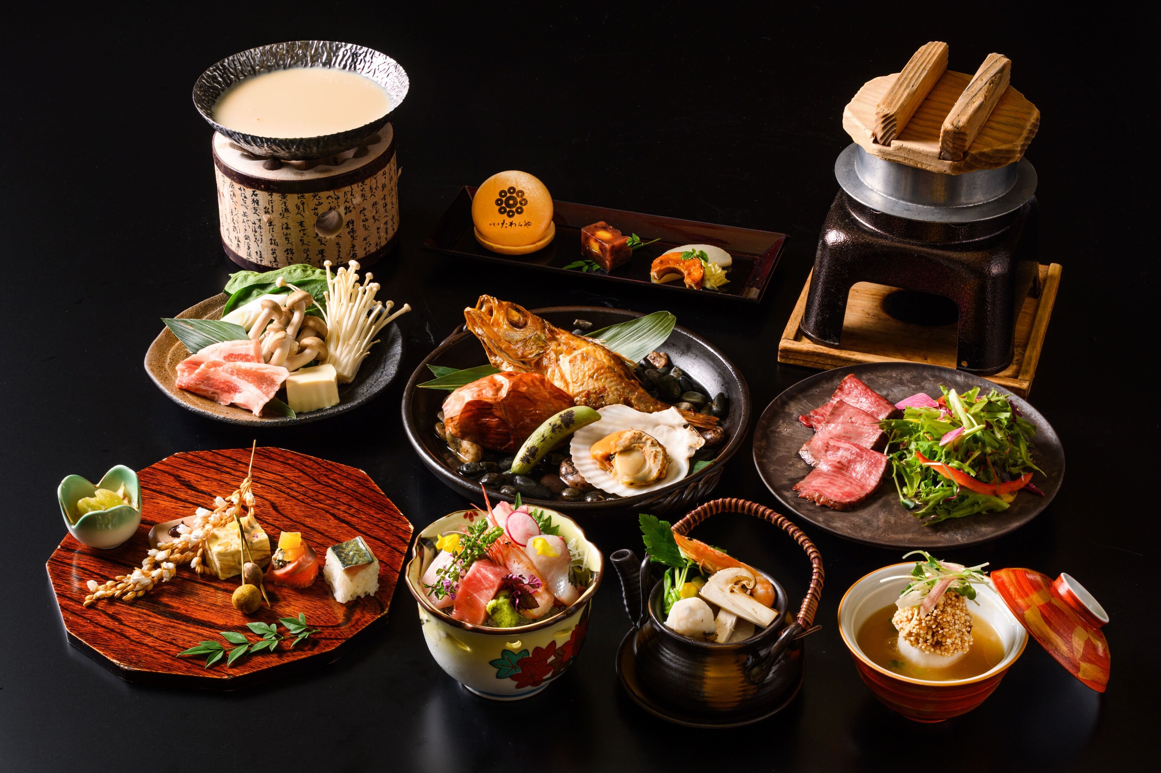 Diversos platos japoneses, incluyendo sushi, sashimi y una olla caliente, dispuestos sobre una mesa negra.