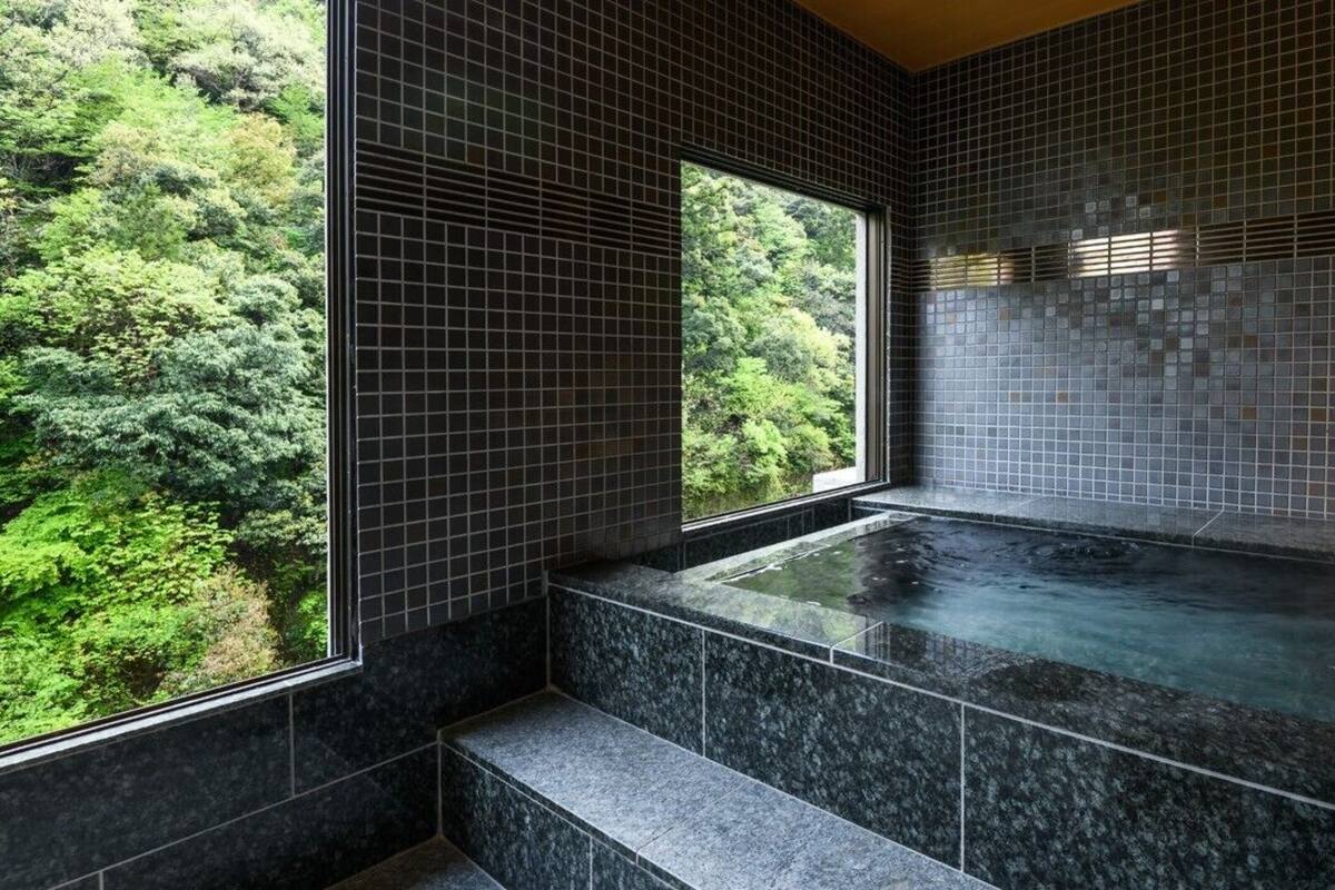 A spa room with a hot tub, tiled walls, and a window overlooking a forest.