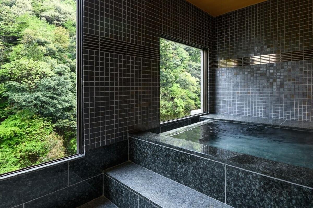 Ett spa-rum med ett bubbelbad, kaklade väggar och ett fönster med utsikt över en skog.