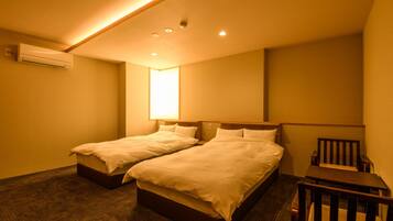 A hotel room with two beds, a small table, and a chair.