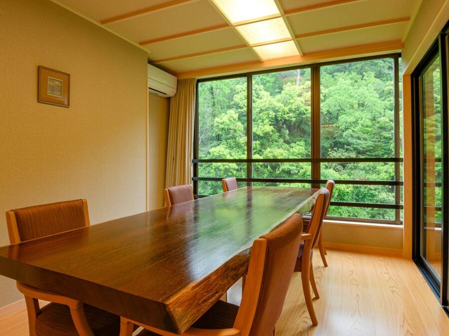 Un salón de conferencias con una larga mesa y sillas, ventanas amplias con vista a un bosque y un cuadro en la pared.