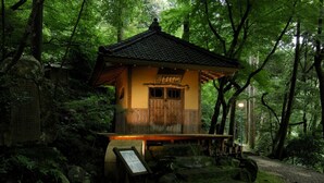 A traditional Japanese wooden structure with a tiled roof, surrounded by dense forest.