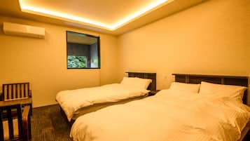 A hotel room with two single beds, a small desk, and a window with a view of greenery.