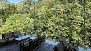 A balcony with a table and chairs overlooking a forested hillside.