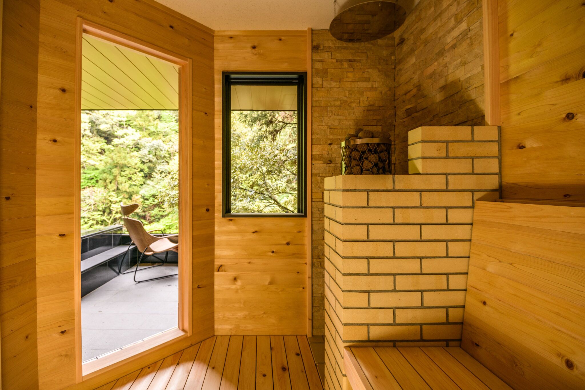 A wooden cabin with a large window, a brick fireplace, and a seating area with a chair.