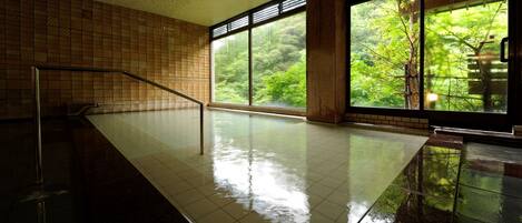A spacious indoor area with a tiled floor, a metal railing, and large windows offering a view of greenery outside.