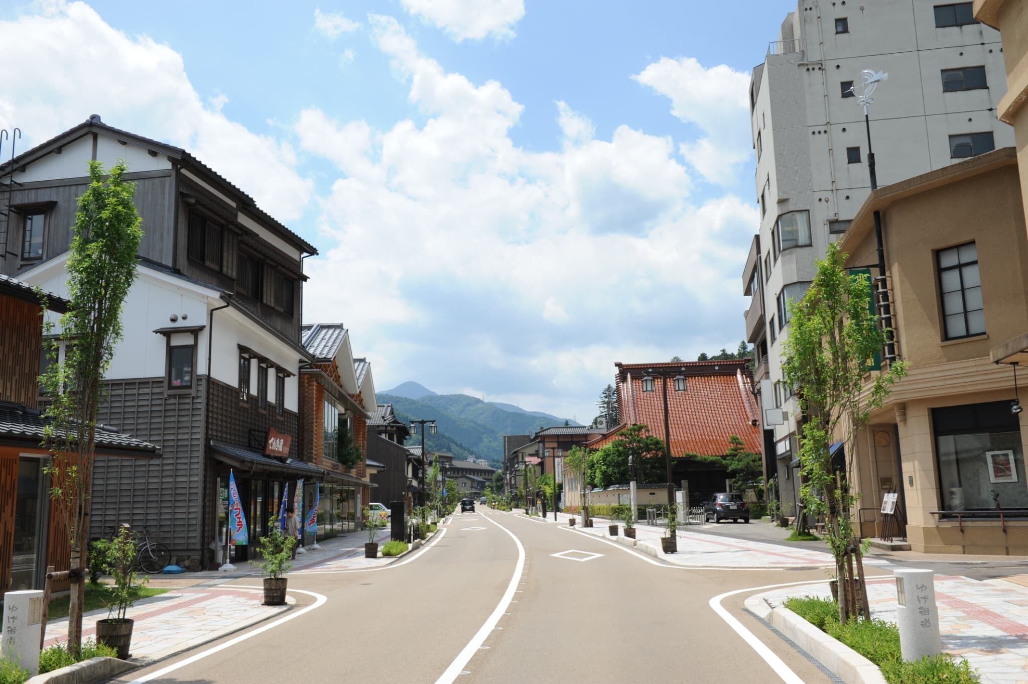 A street lined with traditional and modern buildings, a clear sky, and mountains in the background.