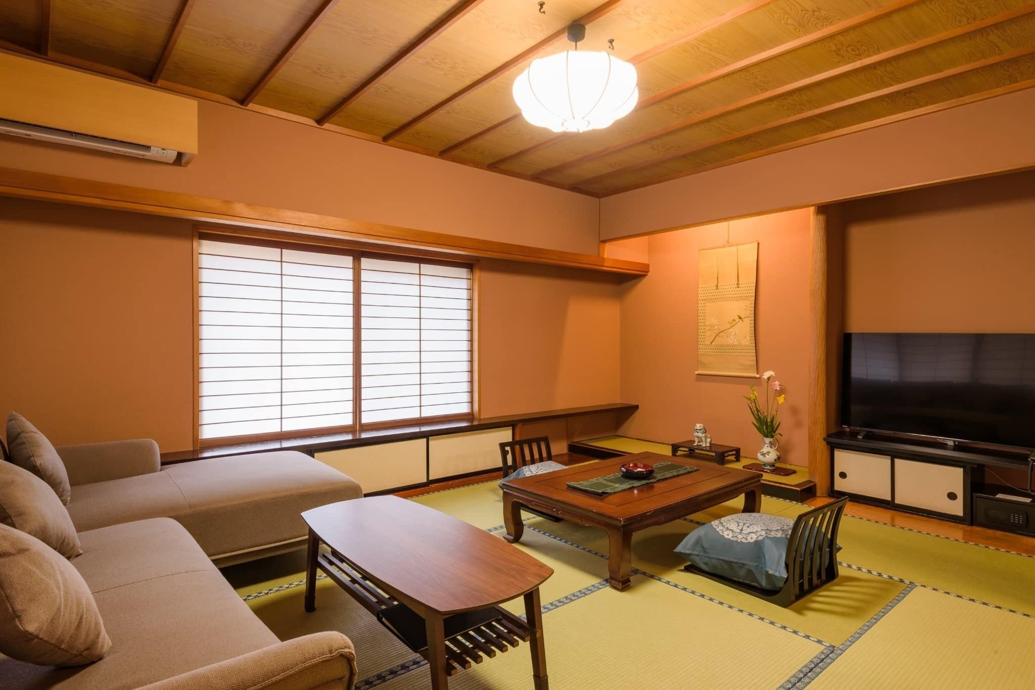 Un salon de style japonais traditionnel, avec un sol recouvert de tatamis, une basse table en bois, un canapé et un téléviseur.