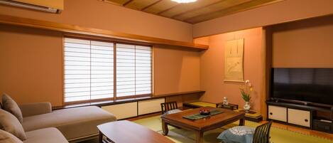 Un salon de style japonais traditionnel, avec un sol recouvert de tatamis, une basse table en bois, un canapé et un téléviseur.