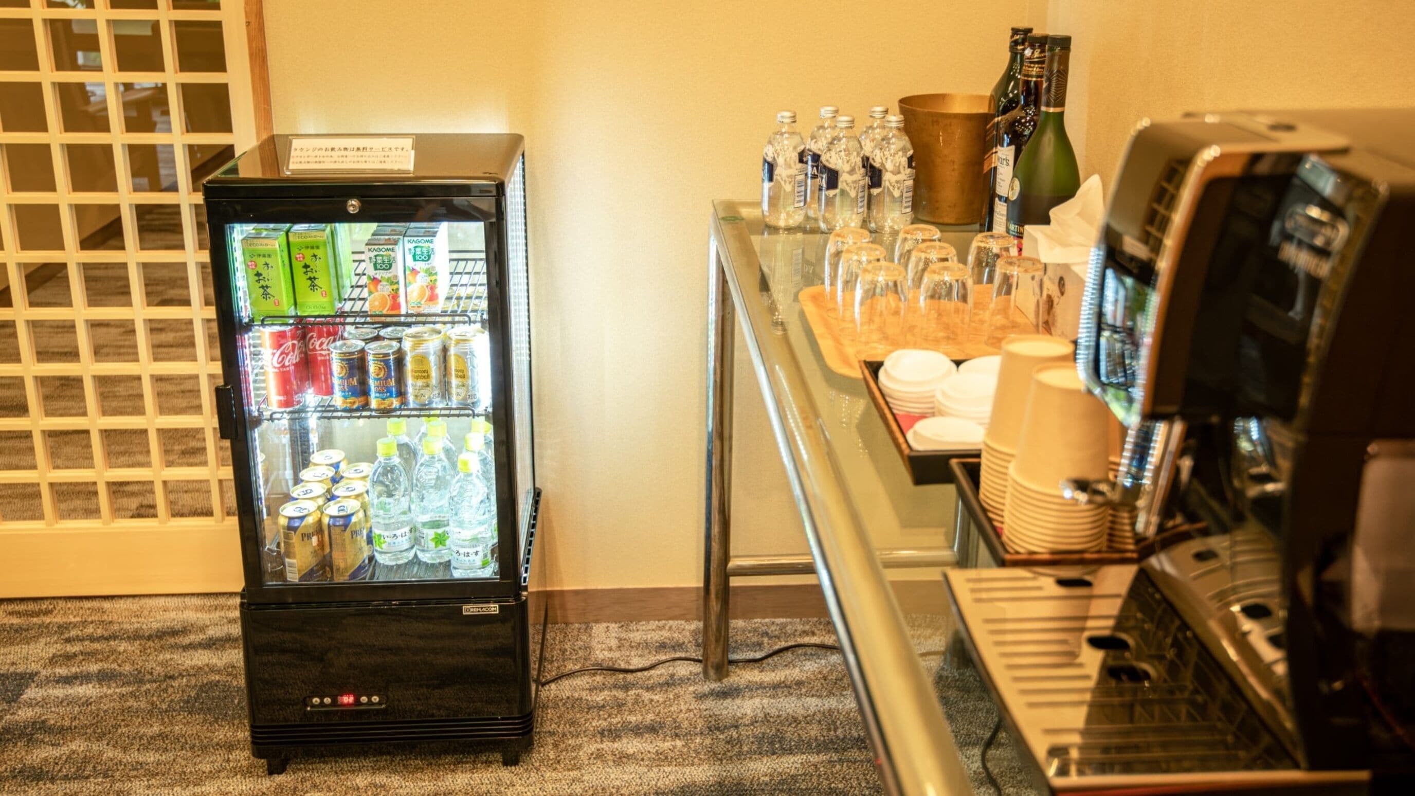 A vending machine with beverages and snacks, a coffee machine, and a table with glasses and bottles.
