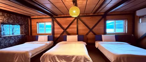 A cabin-style room with three single beds, wooden walls, a stone accent wall, and large windows with a view of the sea.